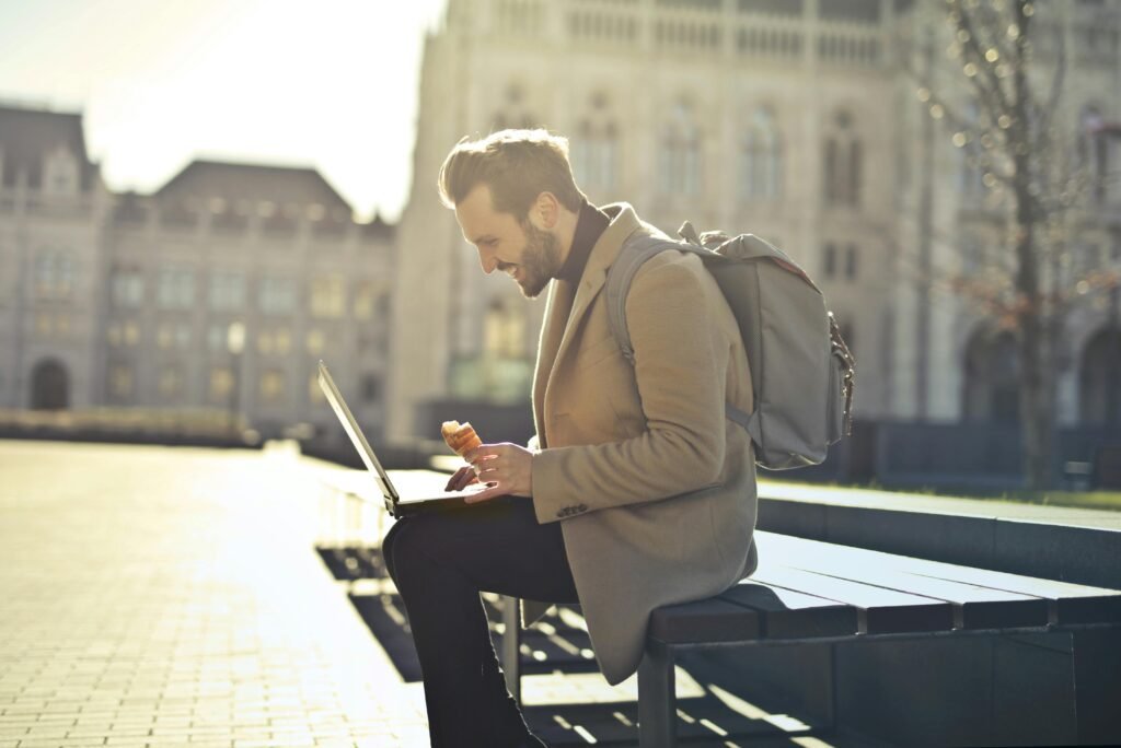 Man working on laptop in Budapest park while enjoying ice cream, showcasing remote work lifestyle.